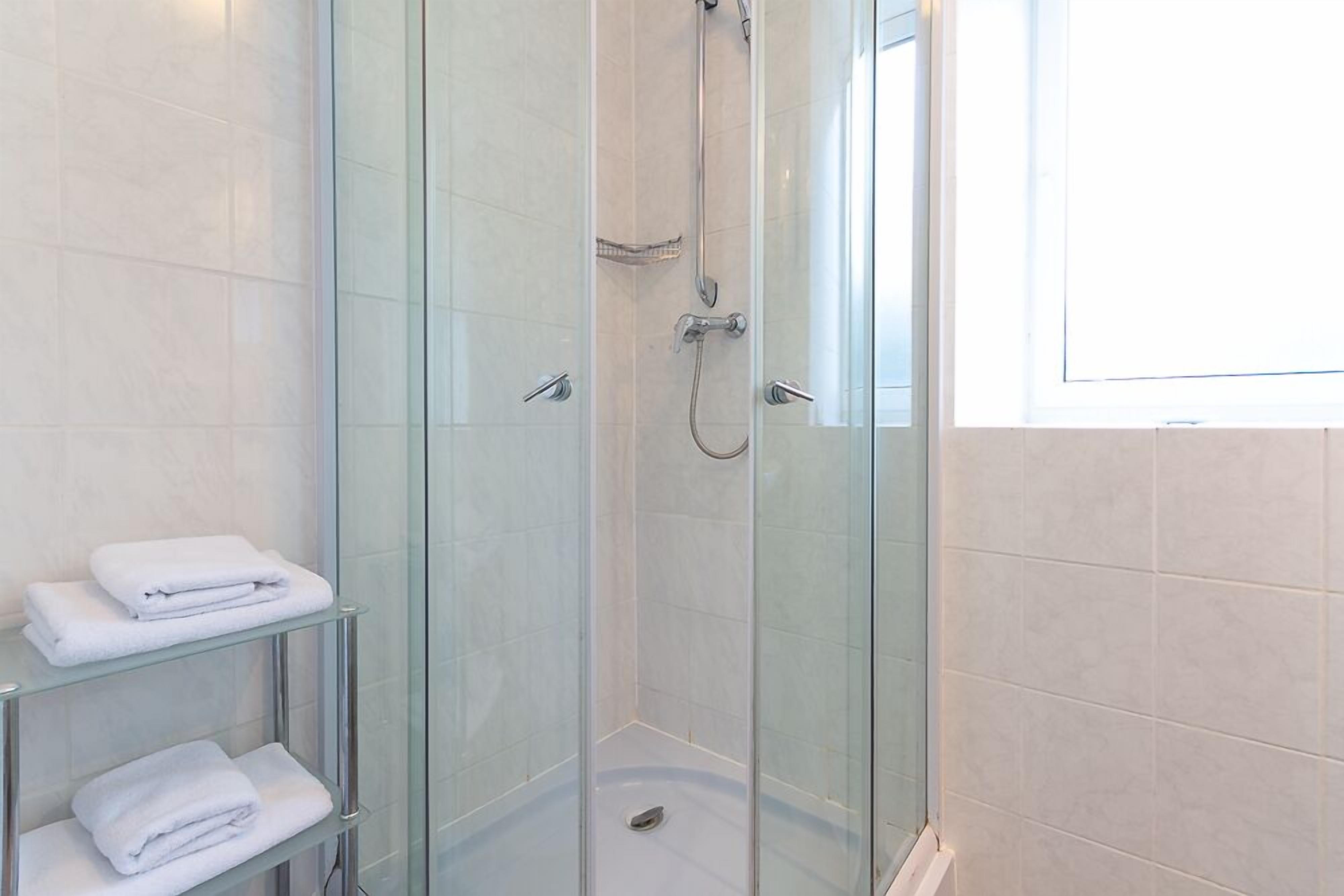 A glass-enclosed shower with a handheld showerhead and a wall-mounted faucet. There are two glass shelves with folded white towels.
