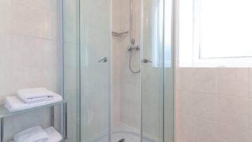 A glass-enclosed shower with a handheld showerhead and a wall-mounted faucet. There are two glass shelves with folded white towels.