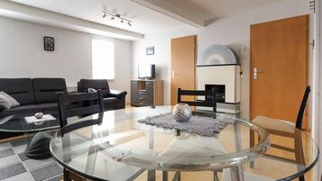 A modern living room with a glass table, black chairs, a black sofa, and a TV stand.