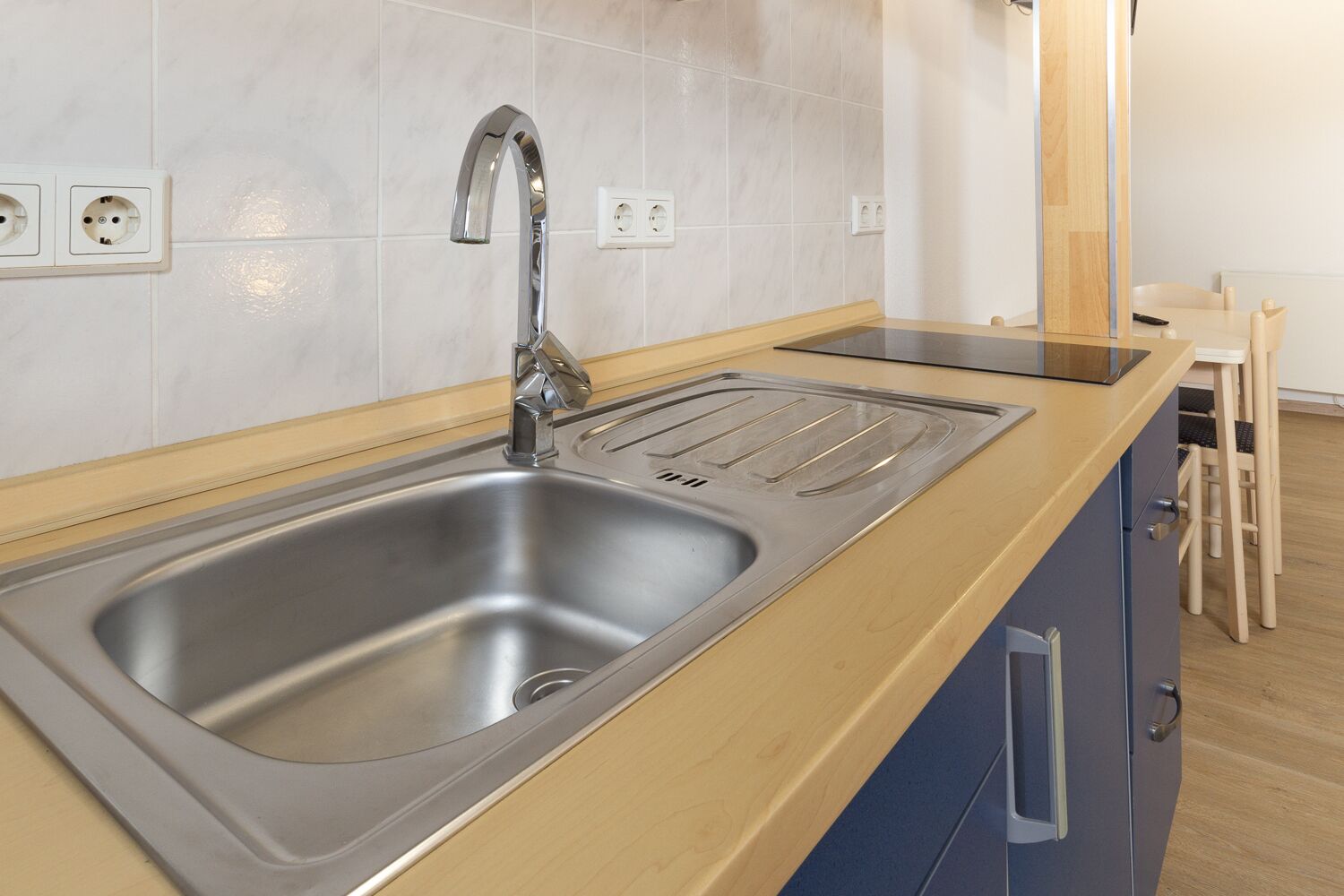 A modern kitchen with a stainless steel sink, wooden countertop, and blue cabinets.