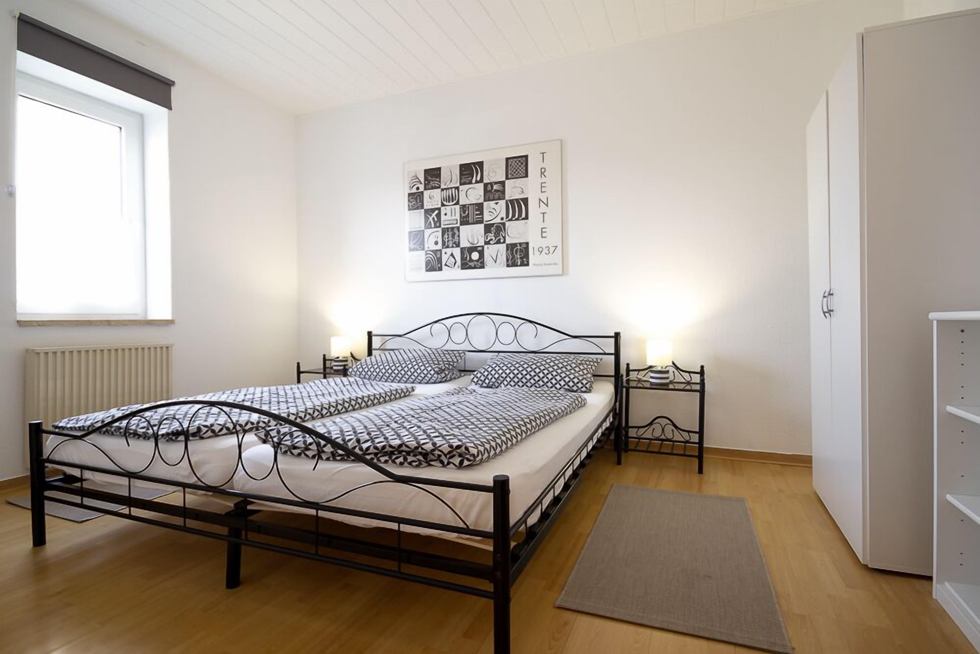 A bedroom with a metal bed frame, a patterned bedspread, a wall art piece, a bedside table, and a radiator.