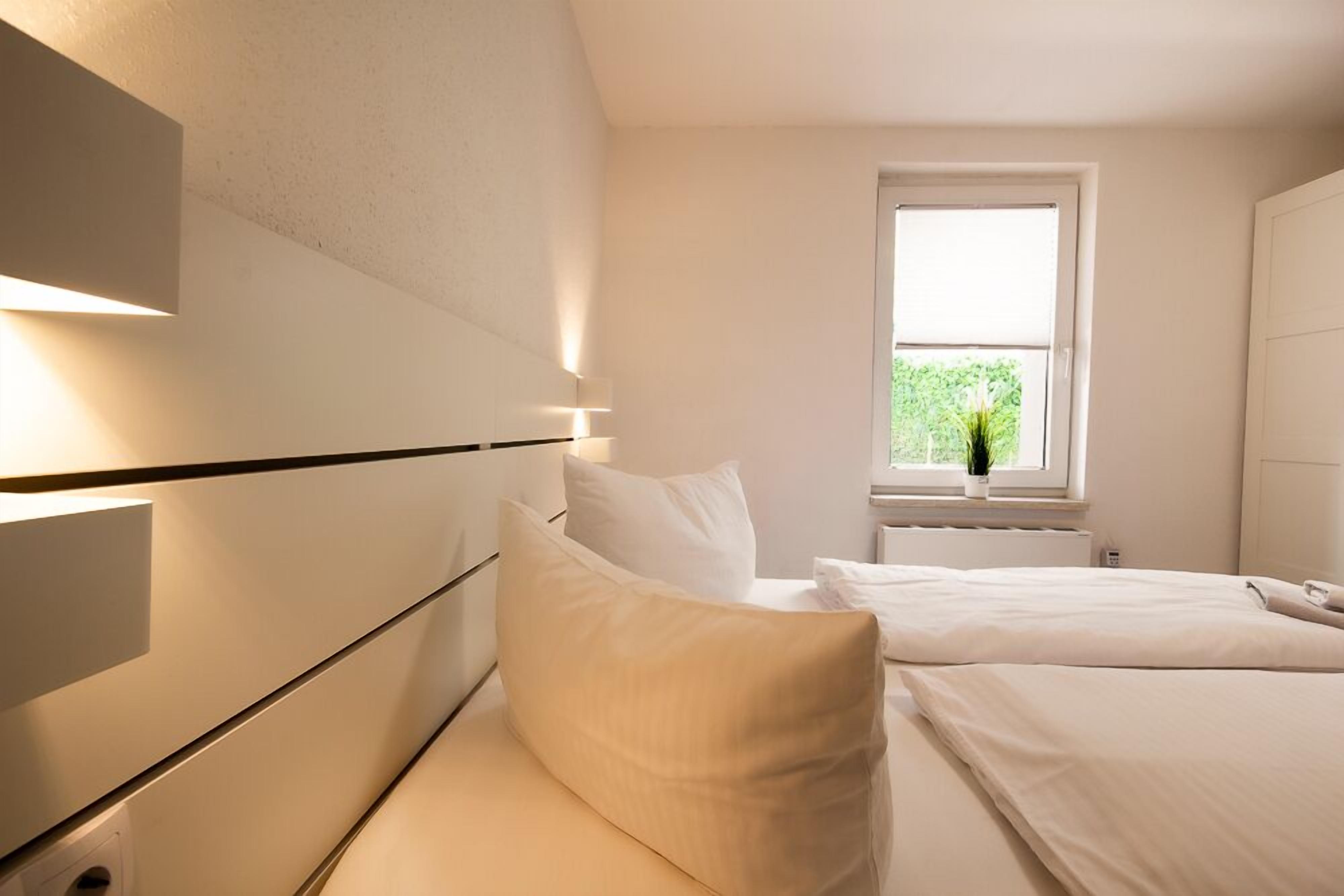 Habitació d'hotel moderna amb llit, taula de nit i finestra amb vista a vegetació.