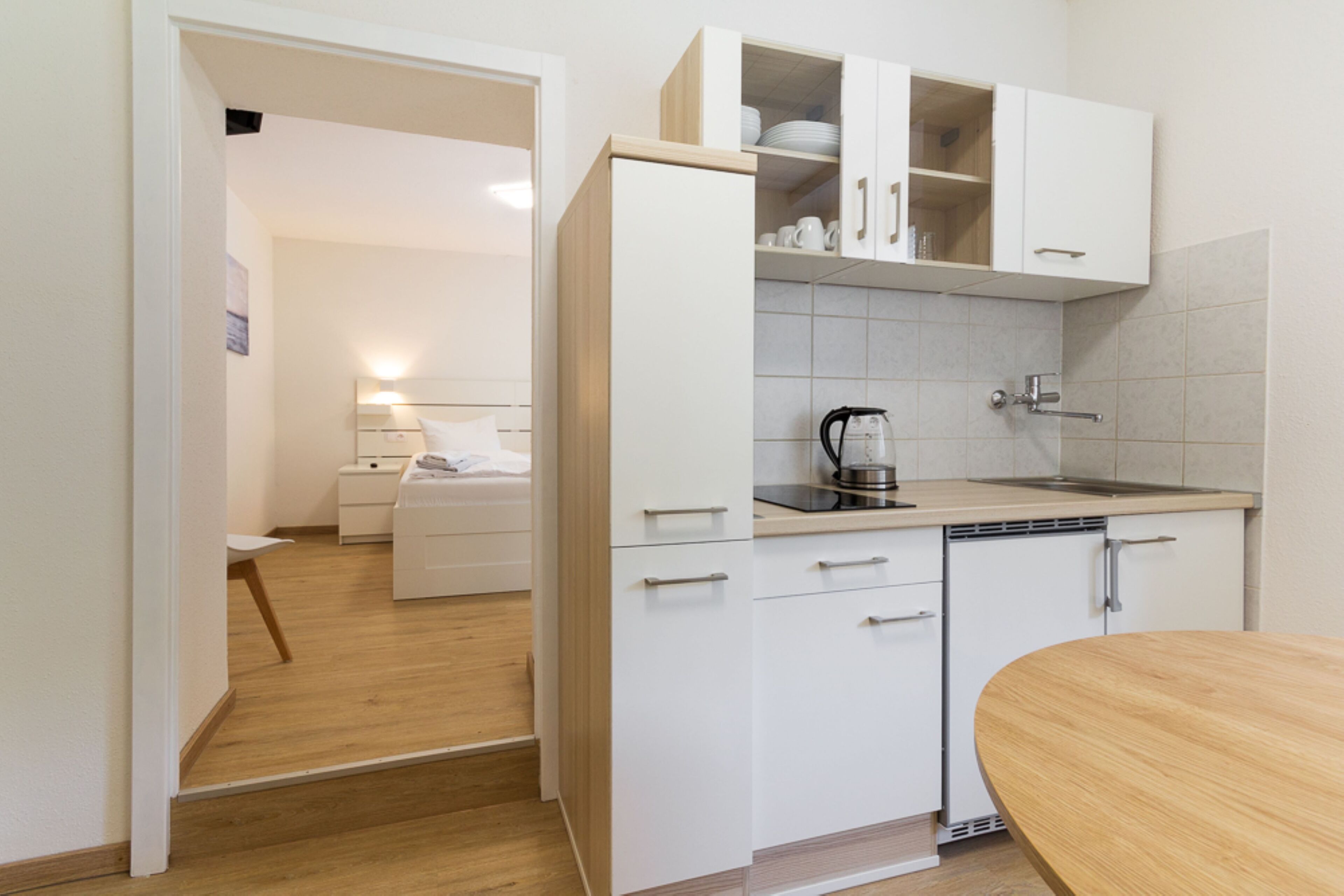 Een kleine keuken met witte kastjes, een koffiezetapparaat en een houten eettafel.