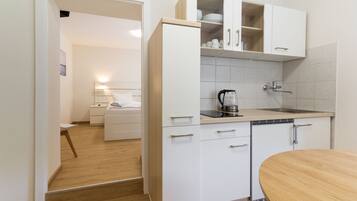 Een kleine keuken met witte kastjes, een koffiezetapparaat en een houten eettafel.
