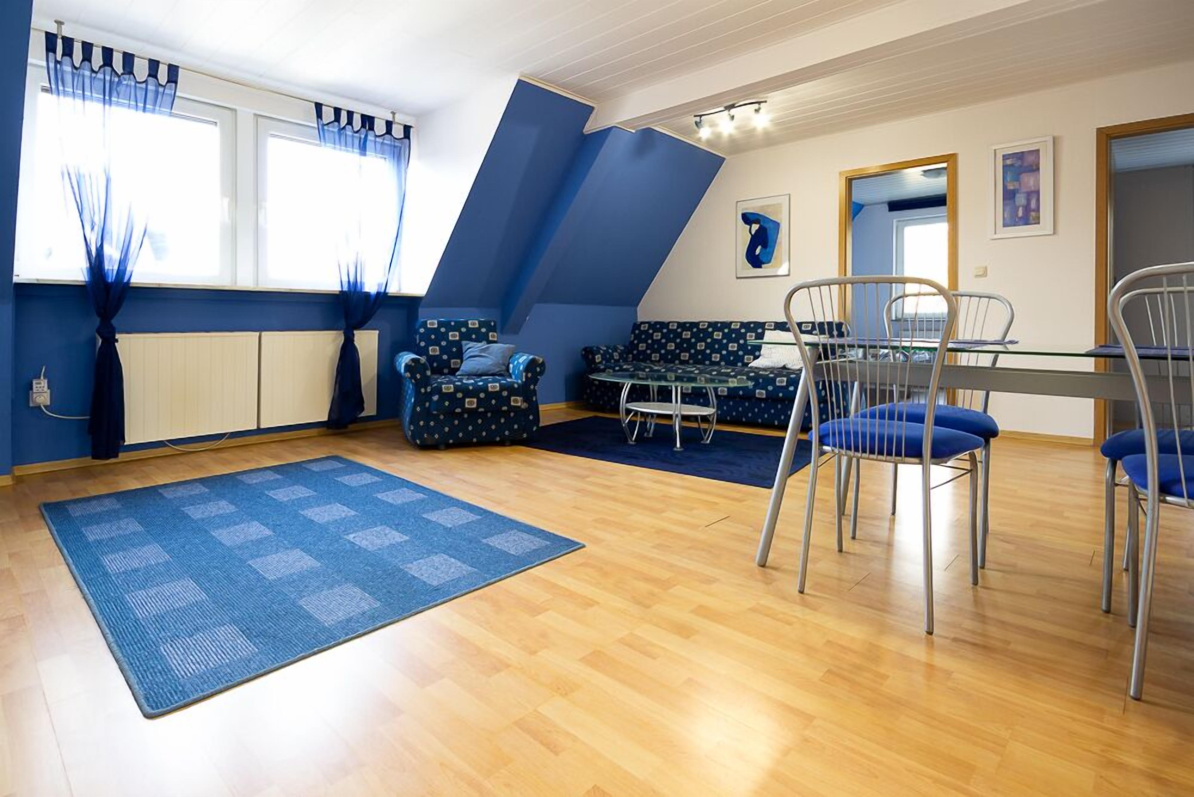 A room with a sloped ceiling, a dining table with chairs, a sofa, and a patterned rug.