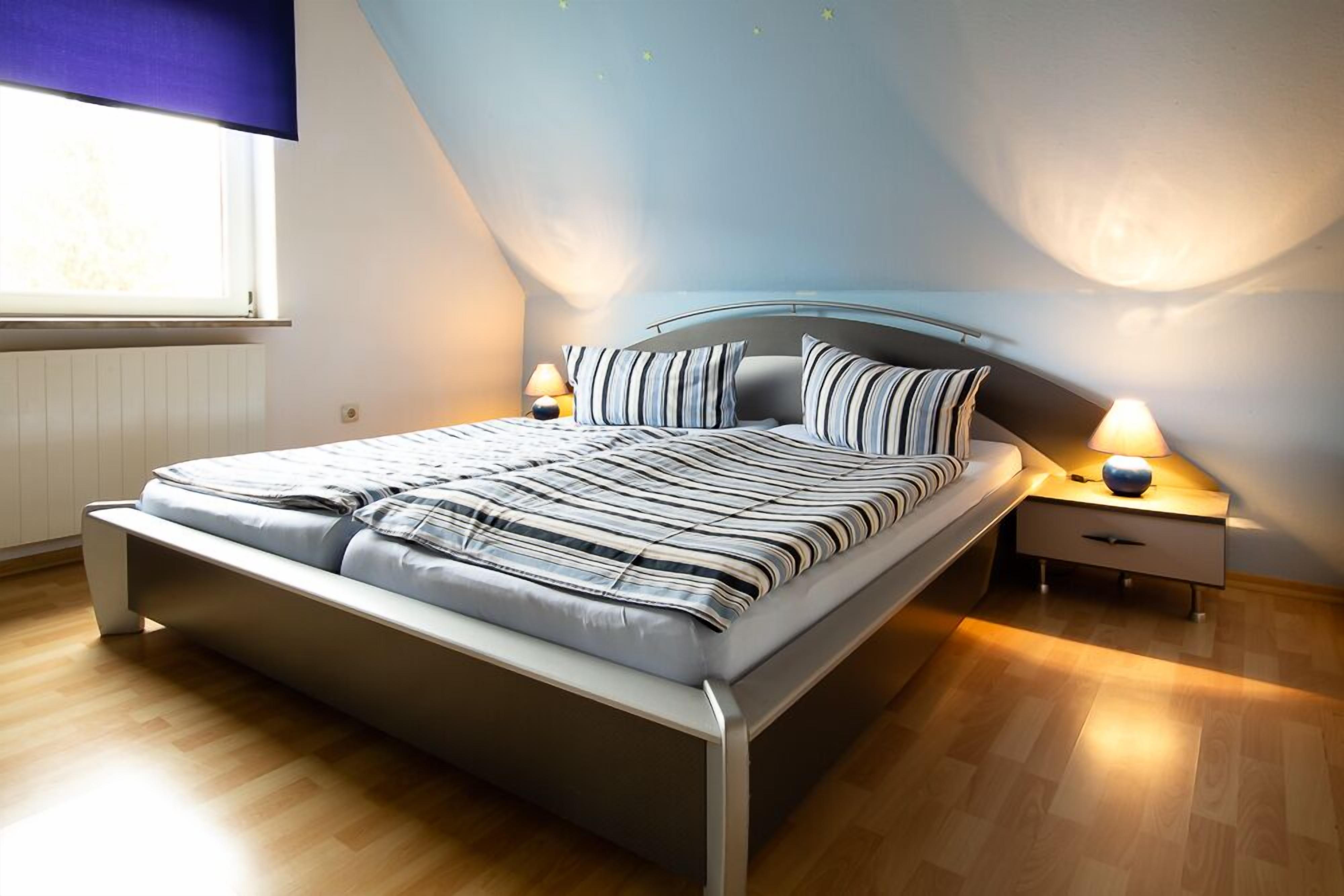 A modern bedroom with a bed, bedside tables, and a window.