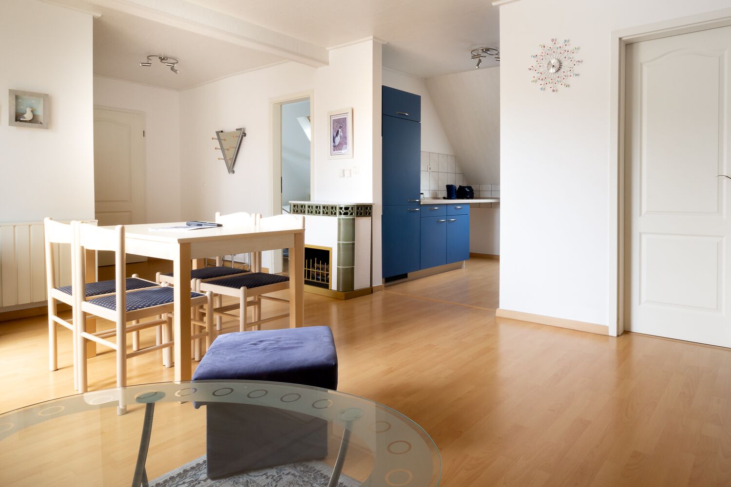 A modern kitchen with blue cabinets, a dining area with a glass table, and a white door.