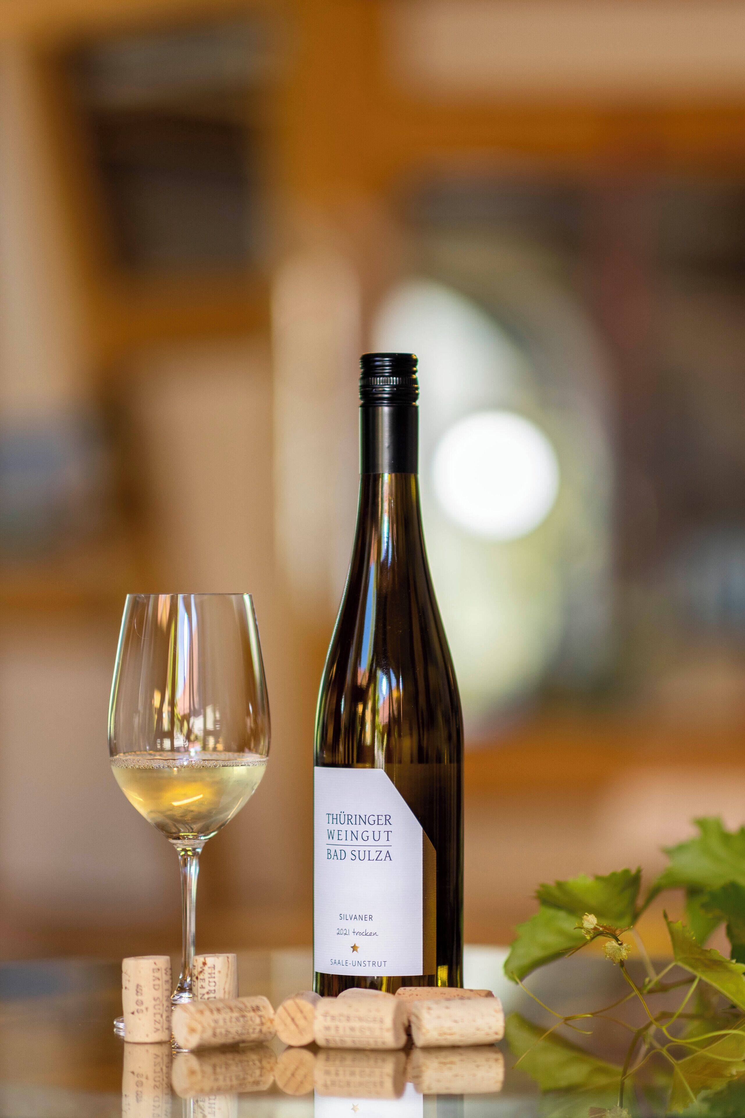 Una bottiglia di vino etichettata "Thüringer Weingut Bad Sulza" e un bicchiere da vino su un tavolo con dei tappi di sughero.