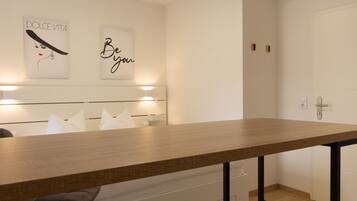 A modern hotel room with a wooden dining table, white headboard, and two wall-mounted light fixtures.