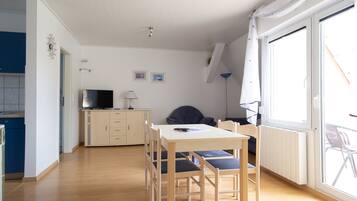 A compact living space with a dining area, a kitchenette, and a large window providing natural light.