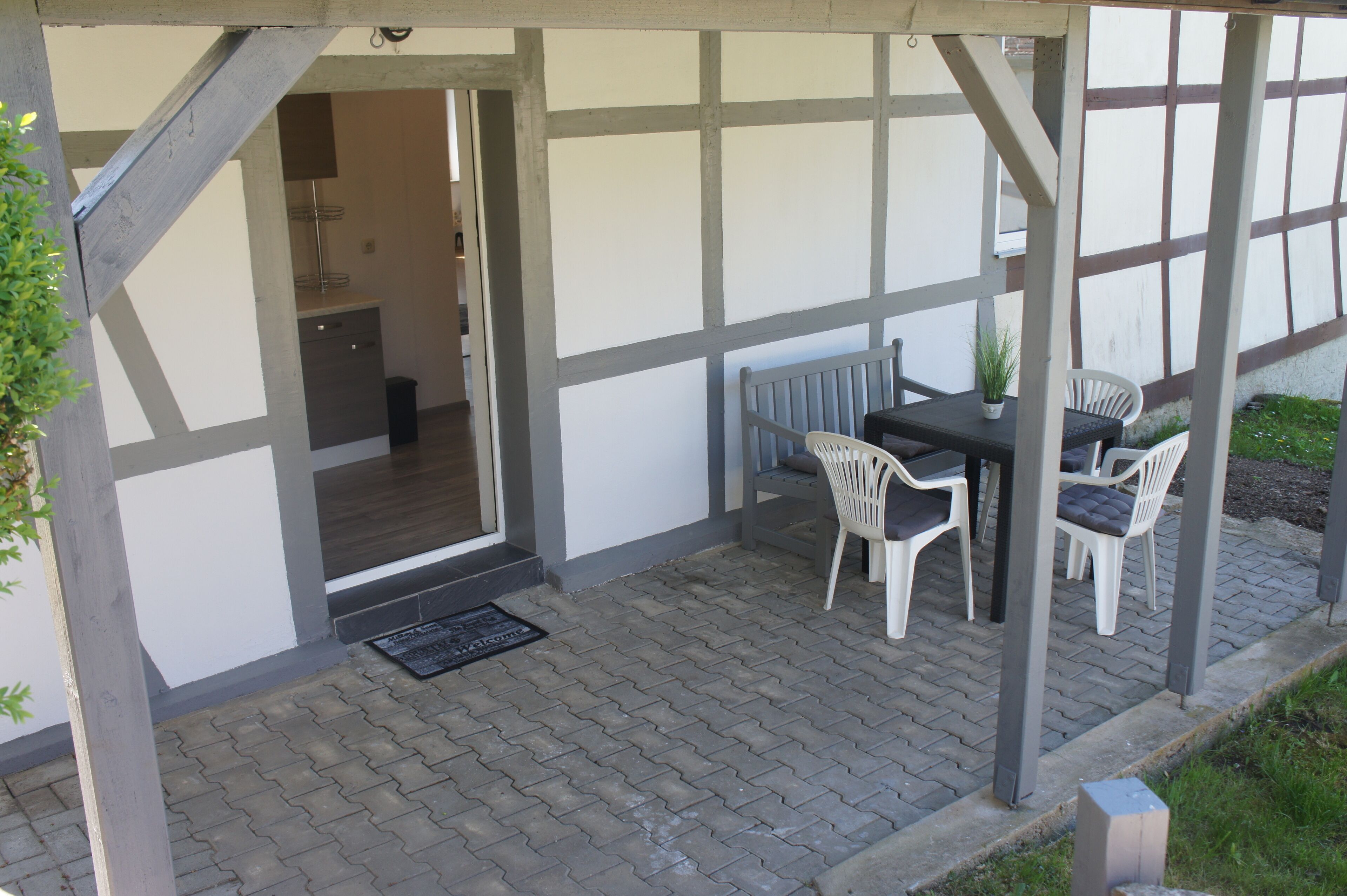 A covered patio area with a table and chairs, a potted plant, and a view into the house.