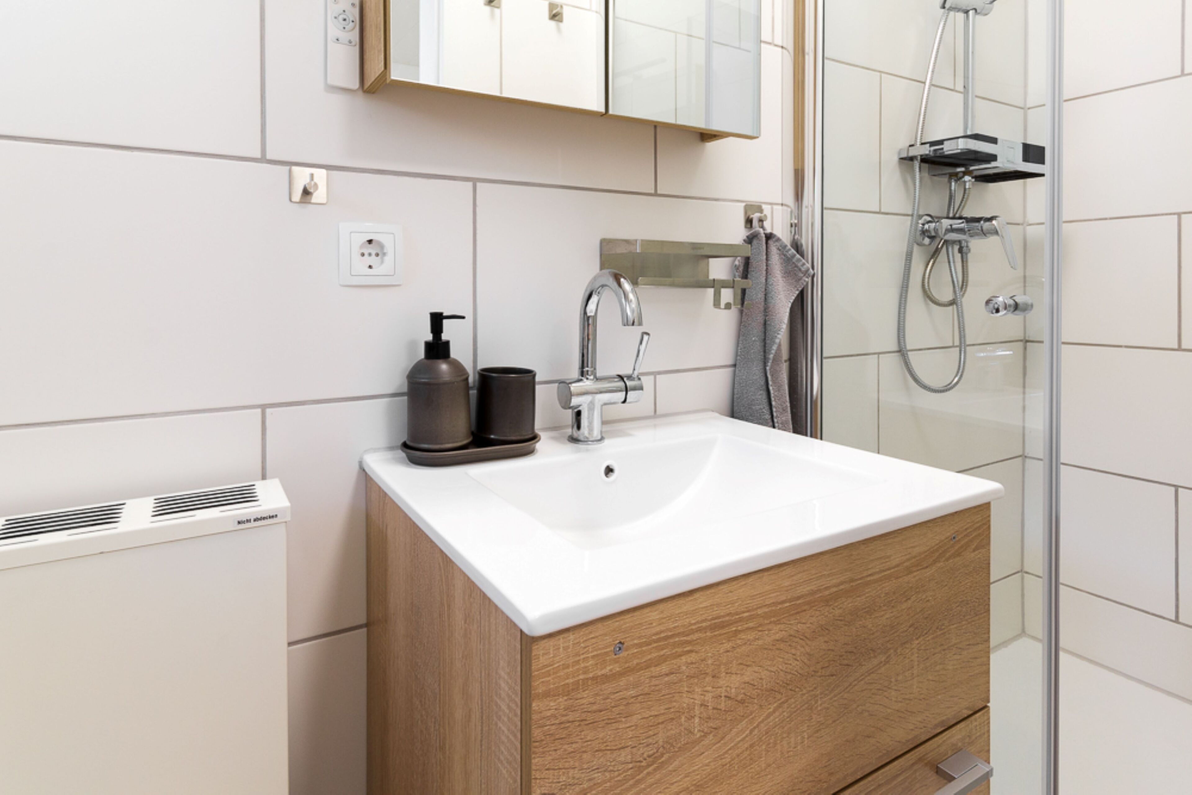 A modern bathroom with a white sink, wooden cabinet, and a glass shower enclosure.