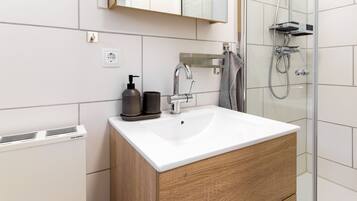A modern bathroom with a white sink, wooden cabinet, and a glass shower enclosure.