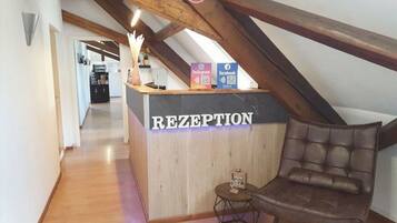 Un comptoir d’accueil portant l’inscription « RÉCEPTION », avec un revêtement en bois, une petite table ronde ornée d’un motif en forme de cœur et un fauteuil en cuir marron.