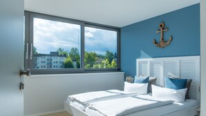 A bedroom with a large window, a bed with white linens, and a blue accent wall. - Ko'Ono Hotel und Restaurant (Konstanz)