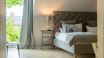 A bedroom with a bed, bedside table, lamp, and a view of greenery outside.