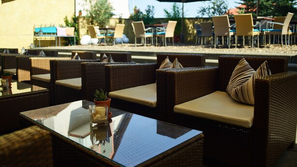 An outdoor seating area with wicker furniture and glass tables, featuring umbrellas and a view of the patio. - Ko'Ono Hotel und Restaurant (Konstanz)