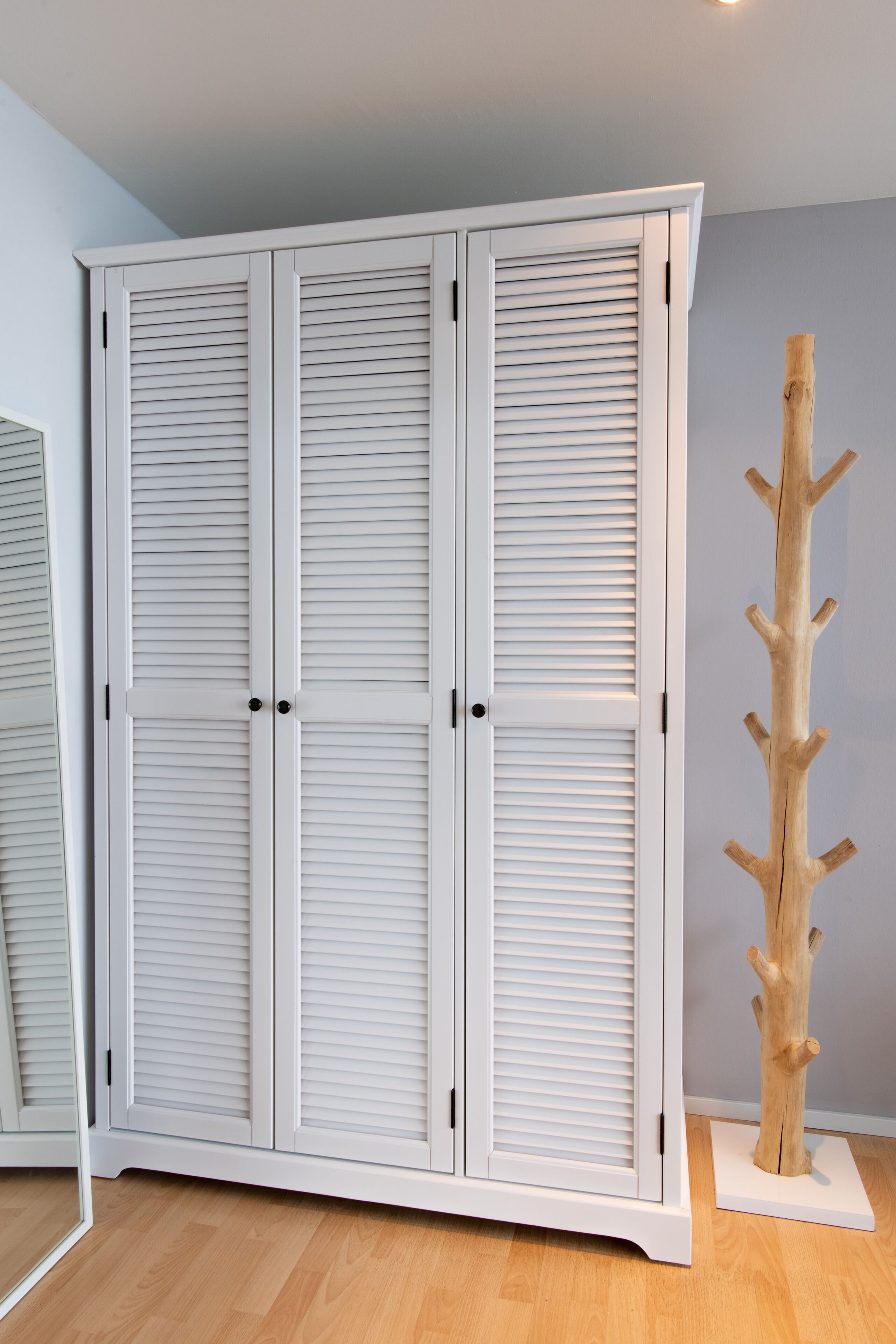 Een witte garderobe met horizontale spijlen en een houten kapstok ernaast.