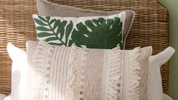A bed with a white and beige striped pillow, a green leaf-patterned pillow, and a white pillow.