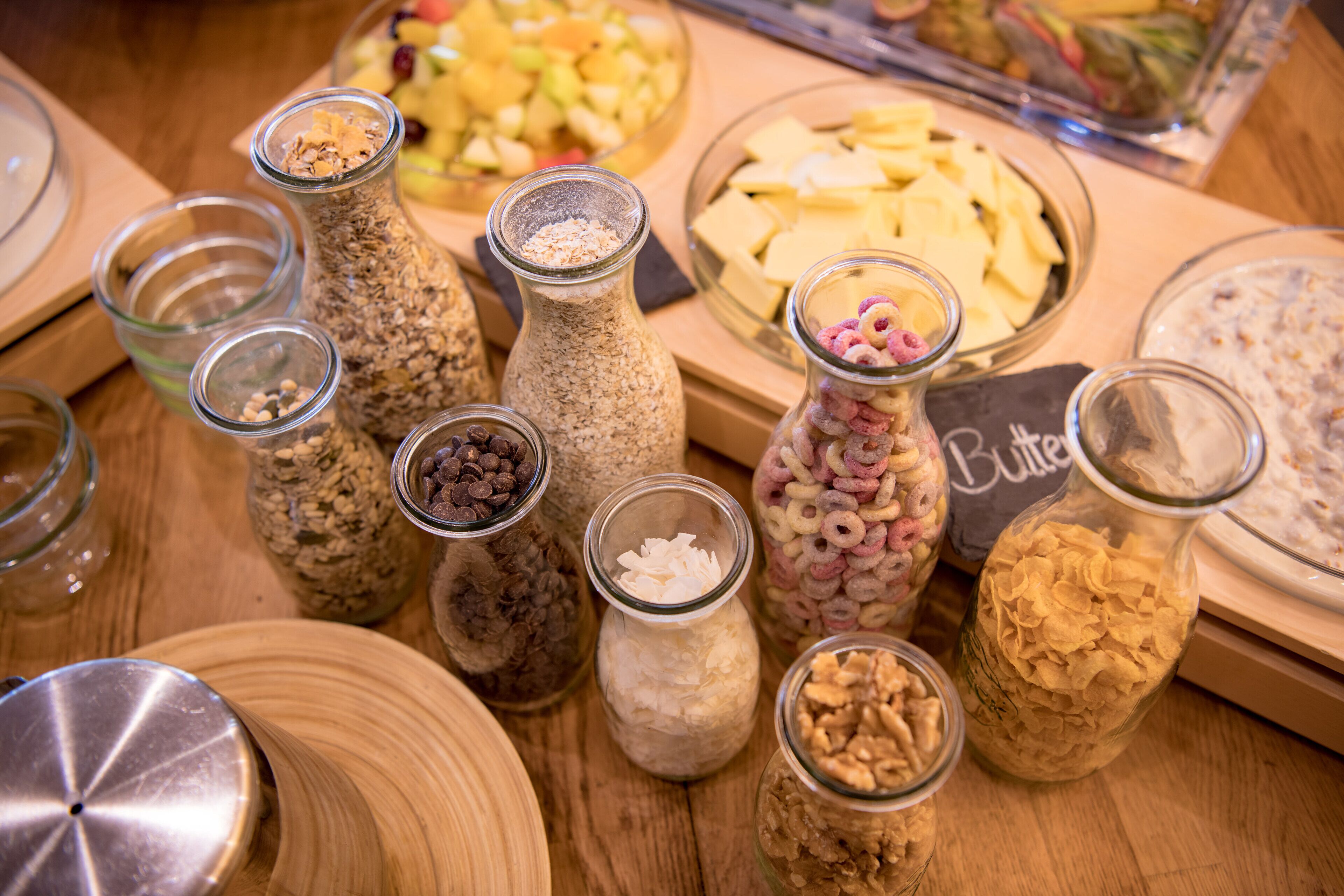 Une variété d’aliments présentés dans des bocaux et des bols en verre, sur une table en bois.