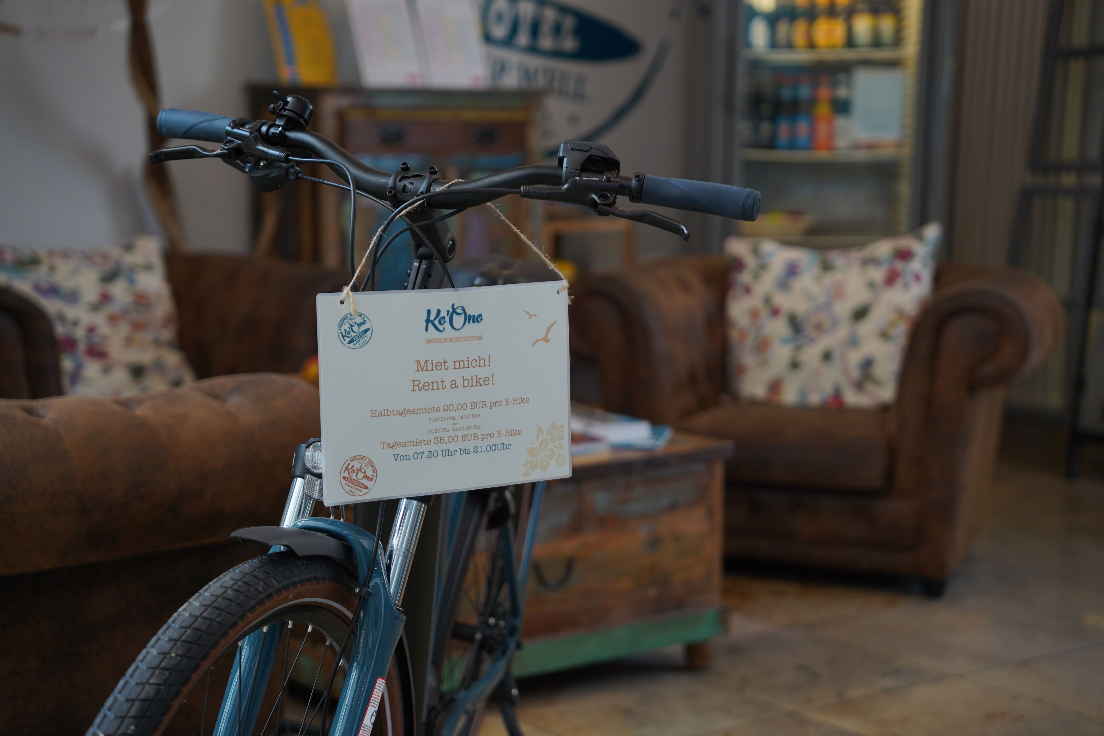 A bicycle with a rental sign in a room with a couch and a wooden chest.