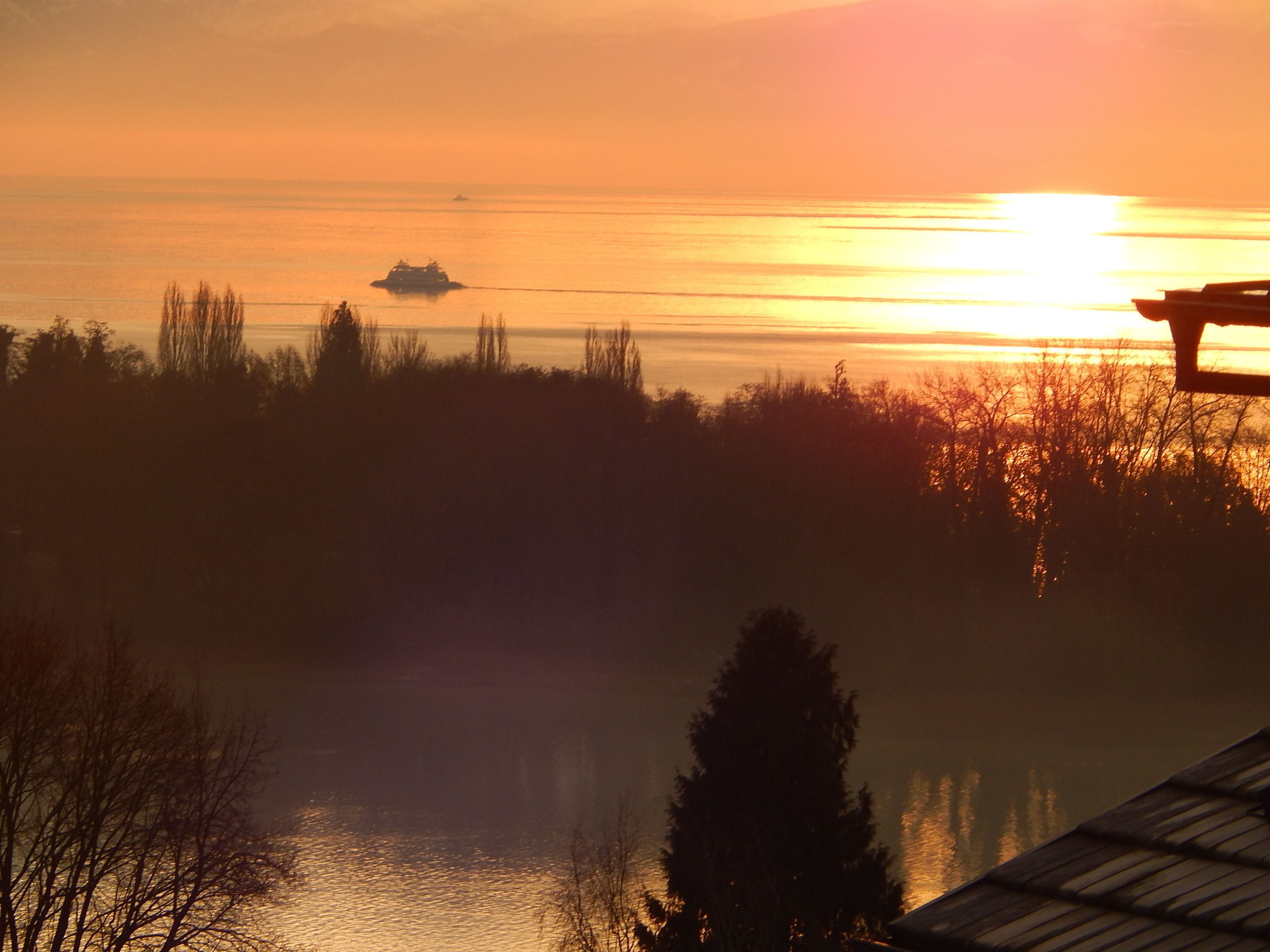 A sunset over a calm body of water with a boat and a dock in the foreground.