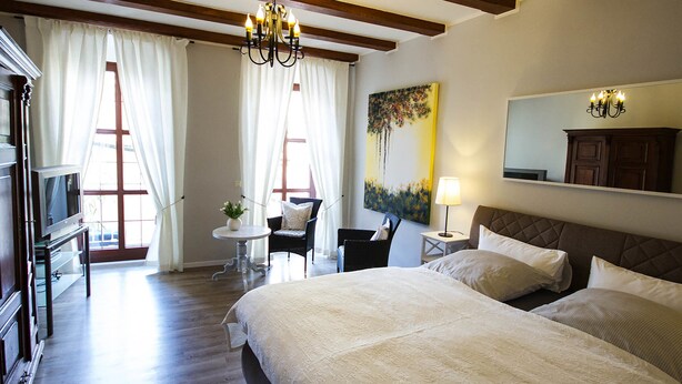 Habitación de hotel con una cama grande, un escritorio con silla, una mesita con lámpara y un cuadro en la pared.
