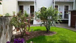 Un patio con un pequeño árbol, un parterre floral y un edificio con balcón.