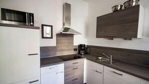 Una cocina moderna con armarios blancos, un lavamanos de acero inoxidable, un microondas y una cafetera.