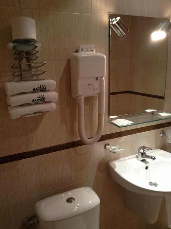 A bathroom with a toilet, sink, and towel dispenser. - Hotel Bansko (Bansko)
