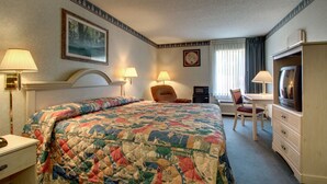 Quarto de hotel com uma cama, uma escrivaninha, uma televisão e duas luminárias.