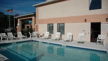 A swimming pool with lounge chairs and a building with a beige facade.