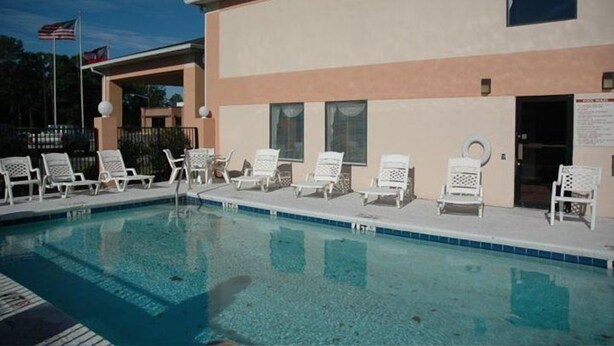 Piscina com espreguiçadeiras e um edifício com fachada bege.