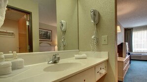 Casa de banho de hotel com lavatório, dispensador de toalhas e secador de cabelo fixado na parede.