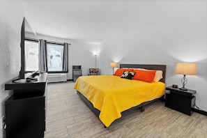 Quarto de hotel com cama, mesas de cabeceira, escrivaninha e janela.