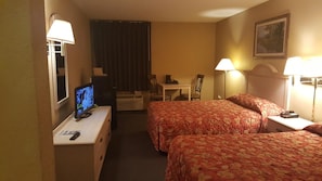 Habitació d'hotel amb dos llits, una escriptori amb televisió, una cadira, una taula i una làmpada.