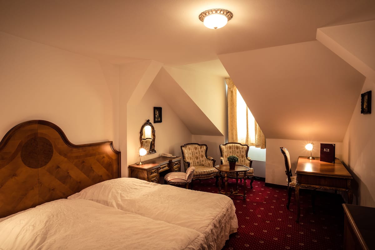 Una habitación de hotel con una cama grande, dos sillones, una mesita y un escritorio con lámpara.