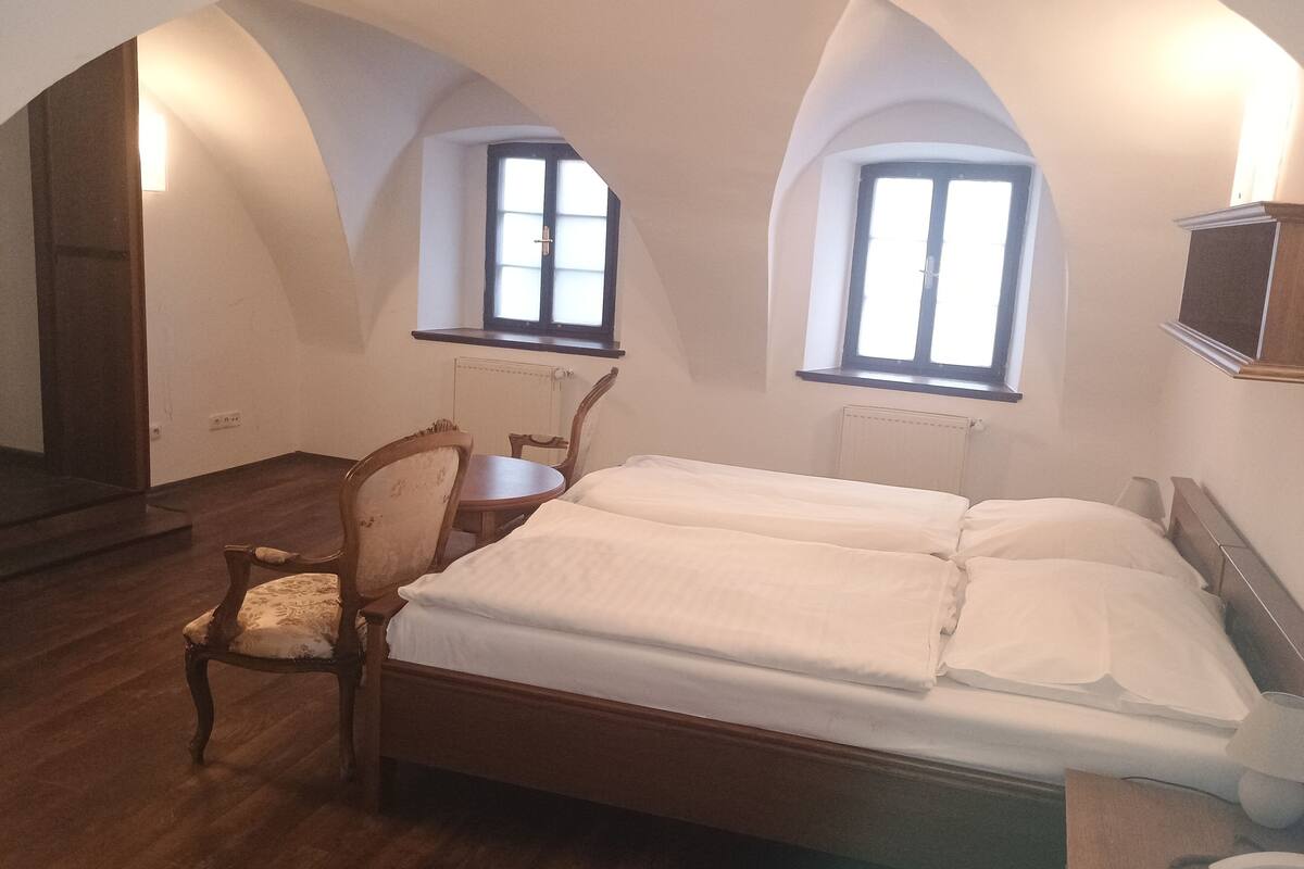 Un dormitorio con una cama de madera, una silla, un escritorio, dos ventanas y un radiador.