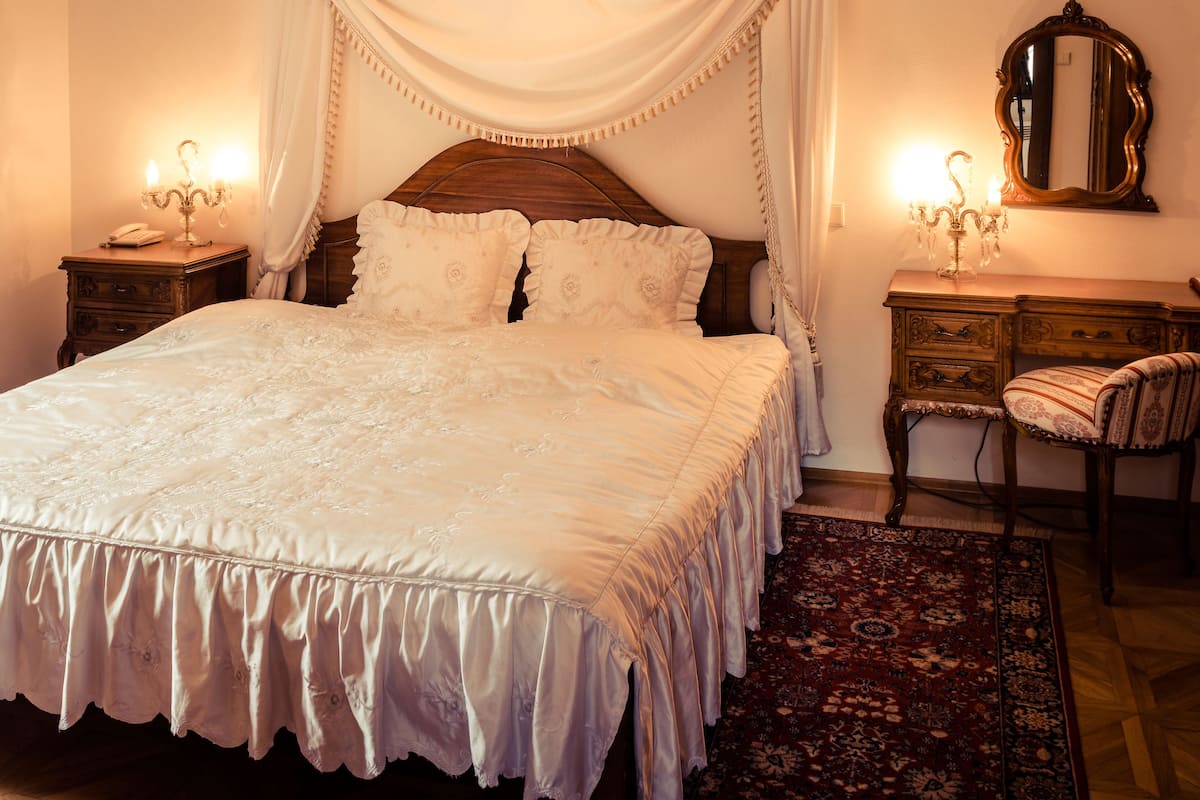 Un dormitorio con una cama grande, una araña, una mesita de noche, una silla y un espejo.
