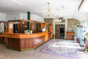 Un vestíbulo con mostrador de recepción, candelabro, pared de piedra y alfombra estampada.