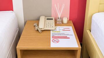 A hotel room with a bedside table featuring a telephone, a candle, and a sign with hotel rules.