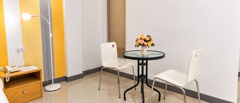 A hotel room with a round table, two chairs, a lamp, a phone, and a window with blinds.