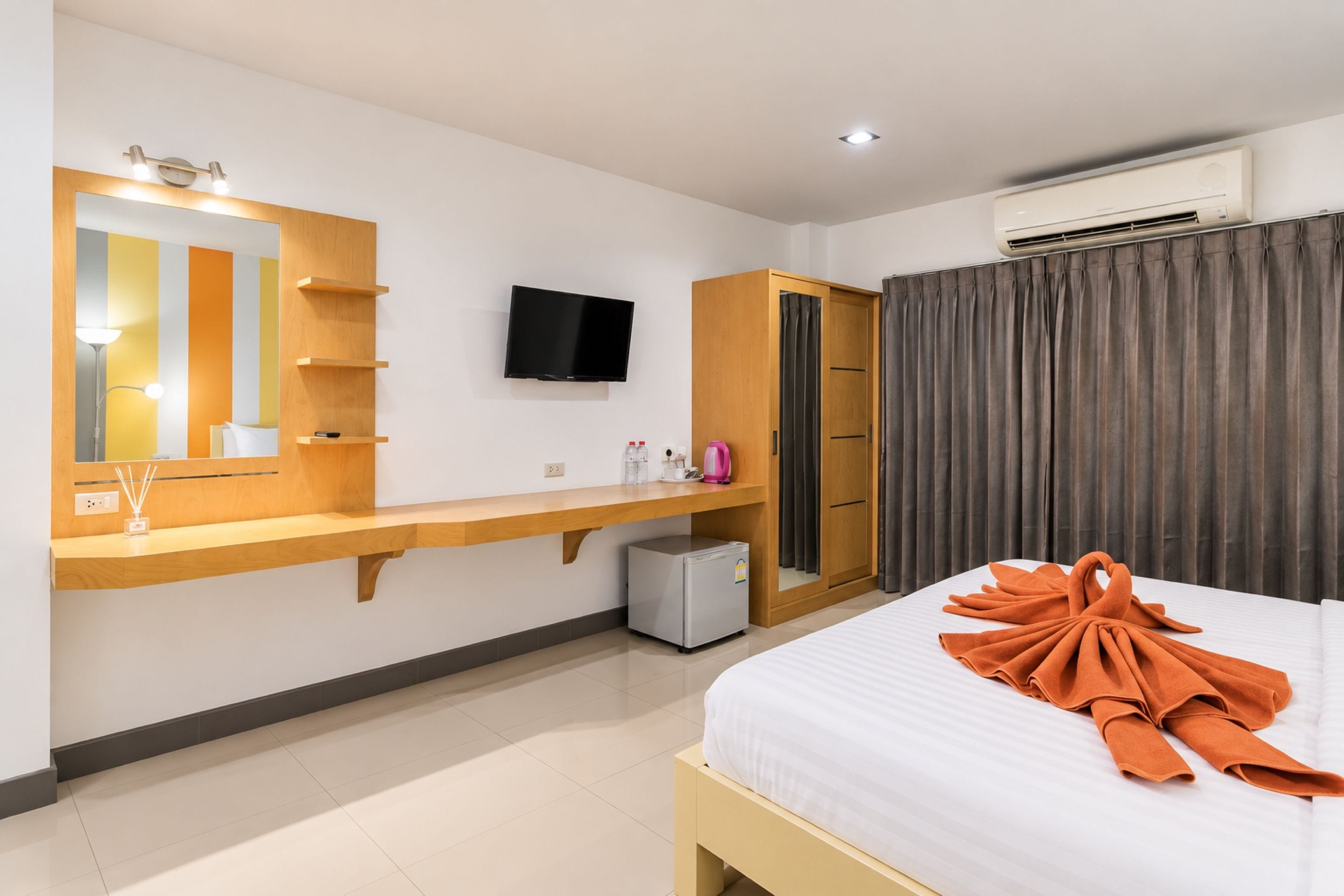 A hotel room with a bed, a TV, a wardrobe, a mirror, a desk, and an air conditioner.