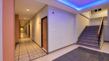 A hotel corridor with a patterned floor, a staircase, and a security camera.