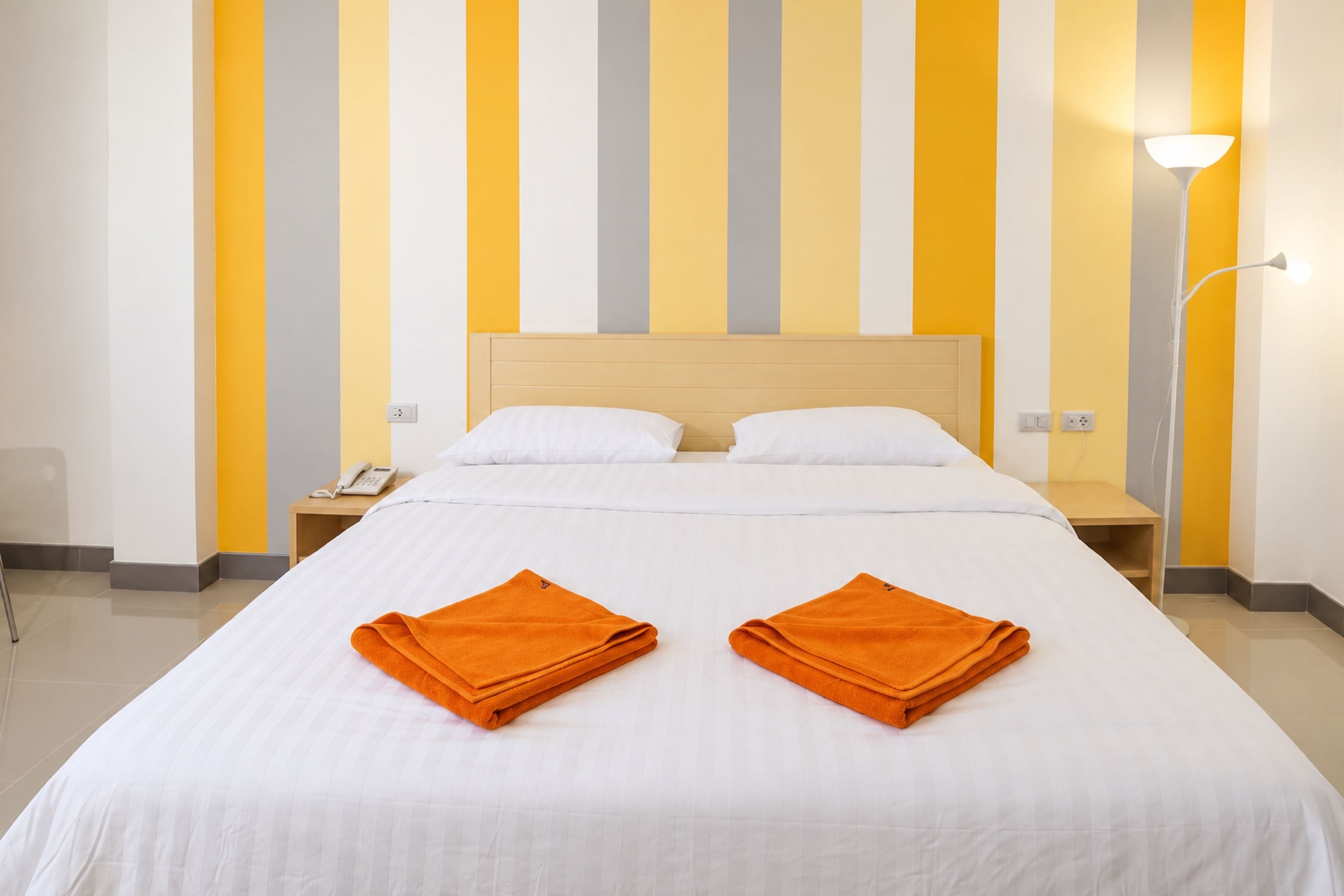 A hotel room with a bed, two folded towels, a bedside lamp, and a phone on the nightstand.
