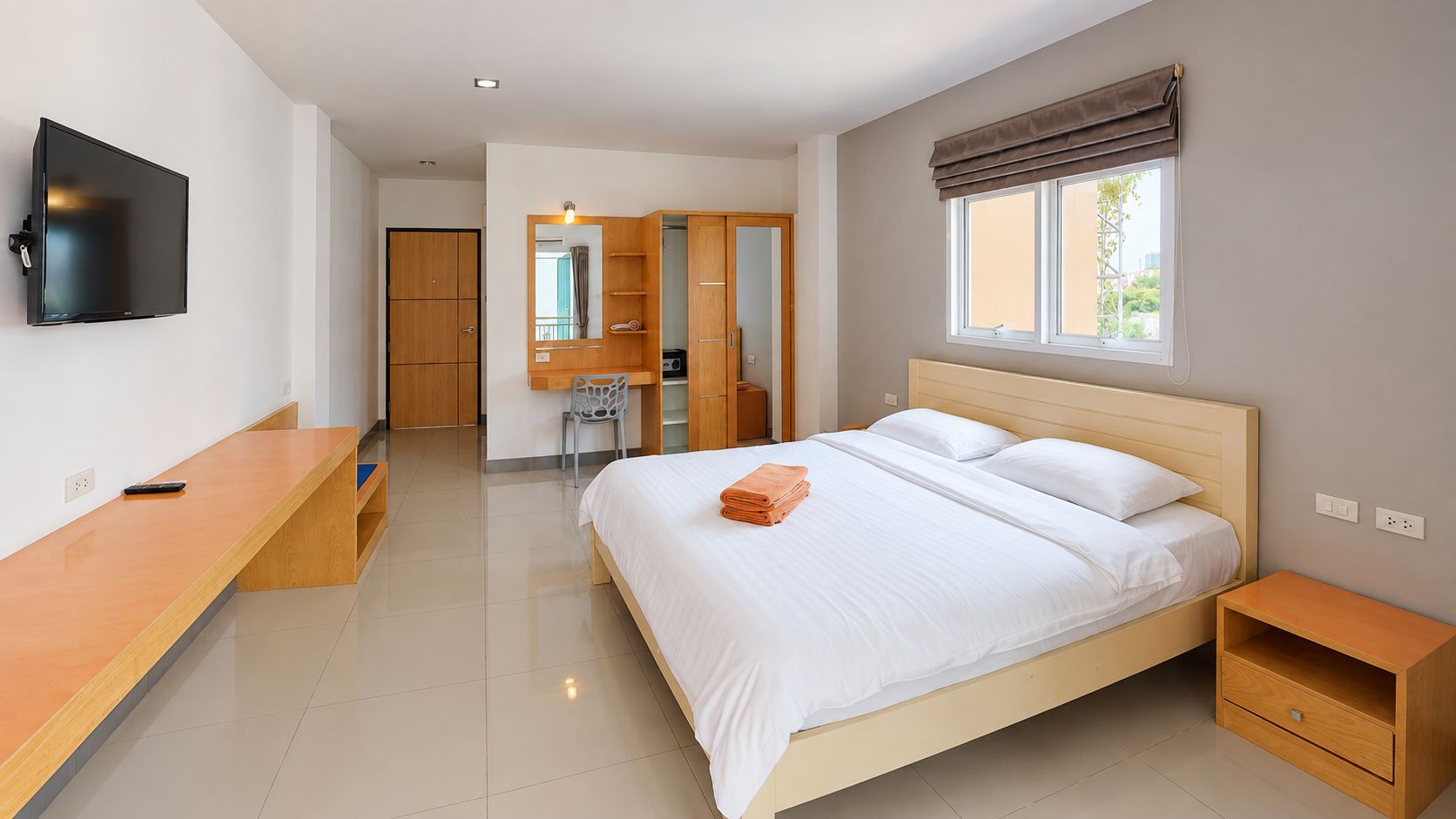 A hotel room with a bed, bedside table, TV, and a desk area.