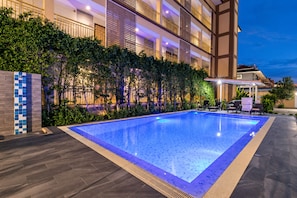 A swimming pool with a tiled border, surrounded by a hedge and a building with multiple balconies. - T Sleep Place (Pattaya)