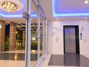 A modern hotel lobby with a glass entrance, a digital elevator display, and a decorative wall. - T Sleep Place (Pattaya)