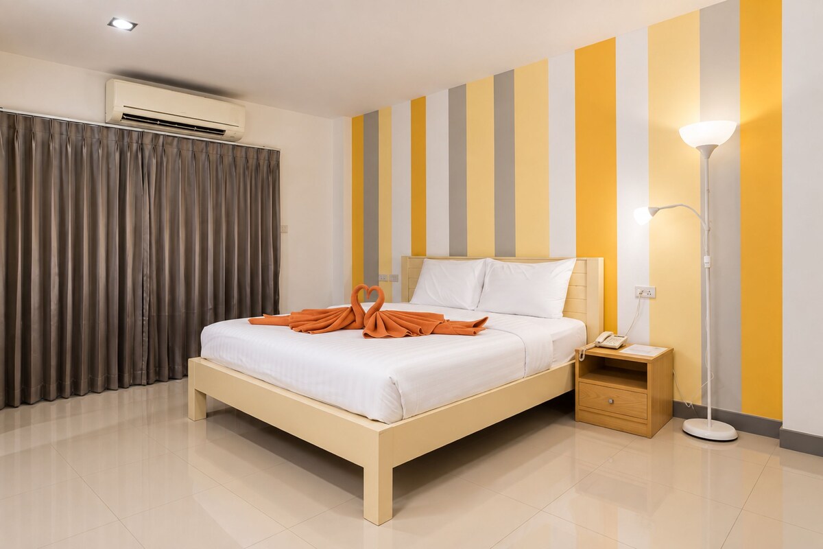 A hotel room with a bed, a bedside table with a lamp, a phone, and a wall with vertical stripes.