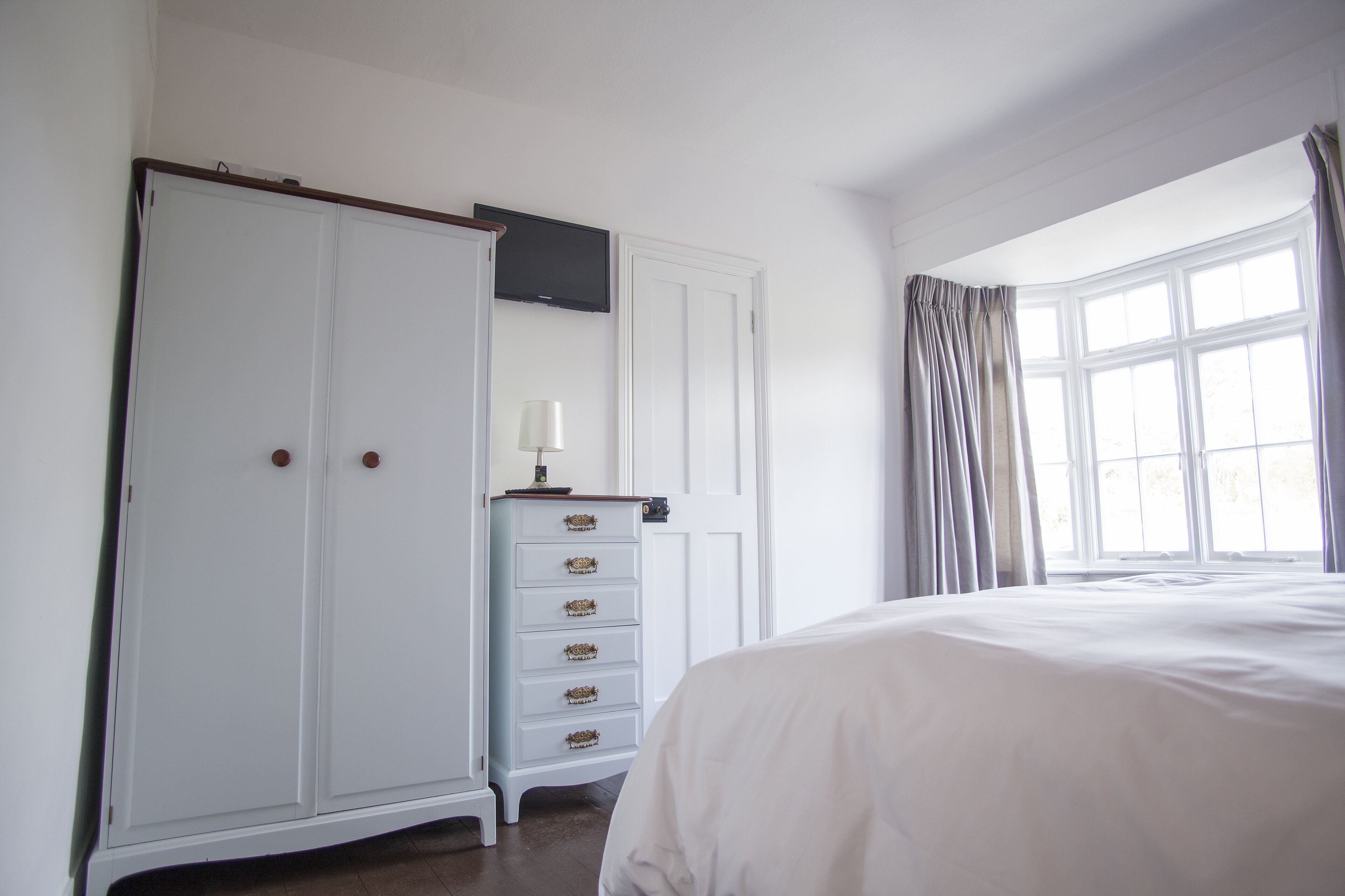 Een slaapkamer met een groot bed, een kledingkast, een dressoir, een televisie en een raam met gordijnen.
